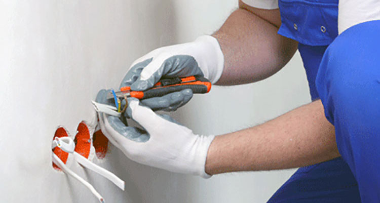 an electricians hands pull wire through outlet holes cut in new sheetrock